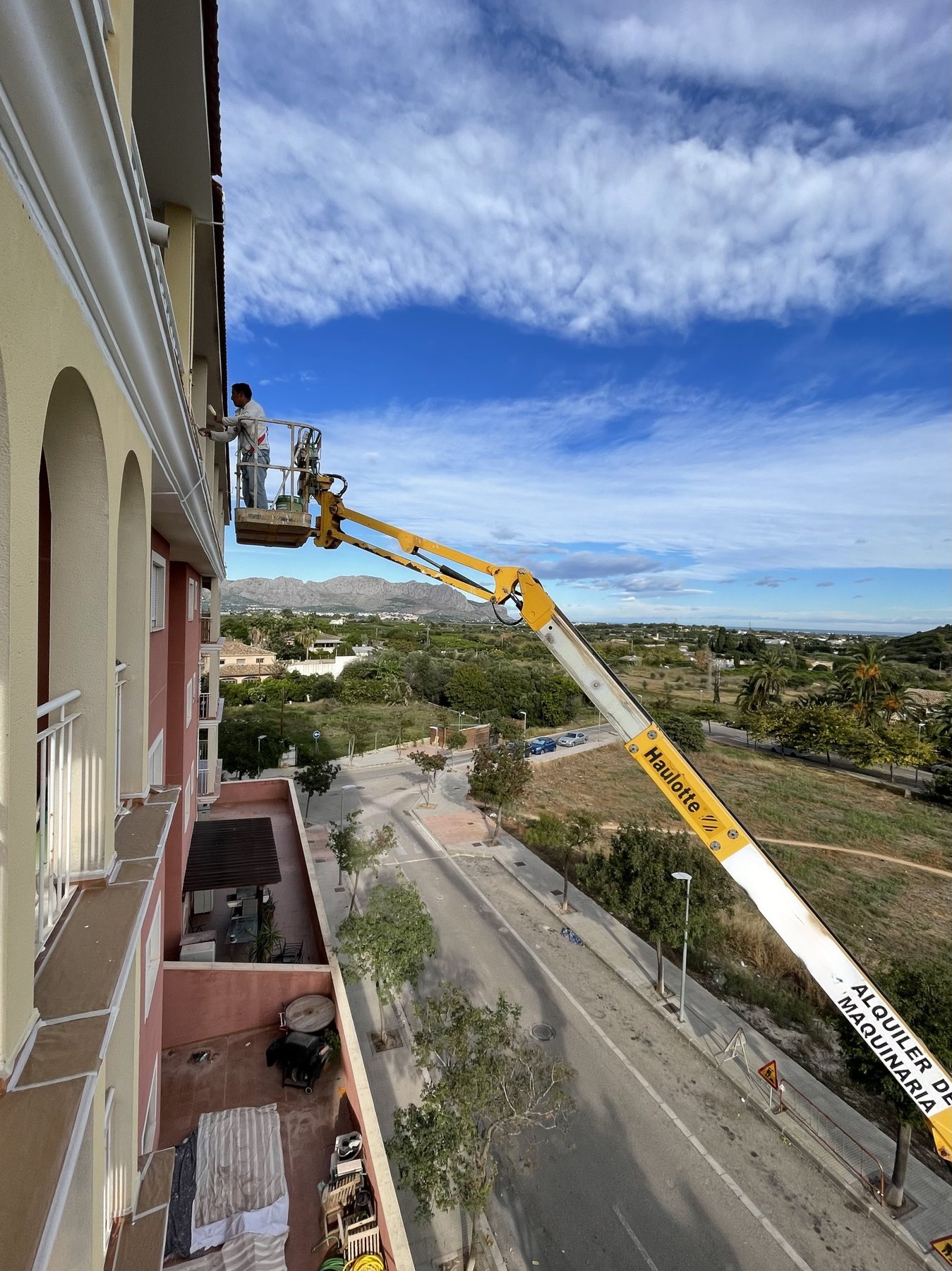 Operario de GUICU pintando fachada de comunidad de vecinos en altura con plataforma elevadora en Pedreguer