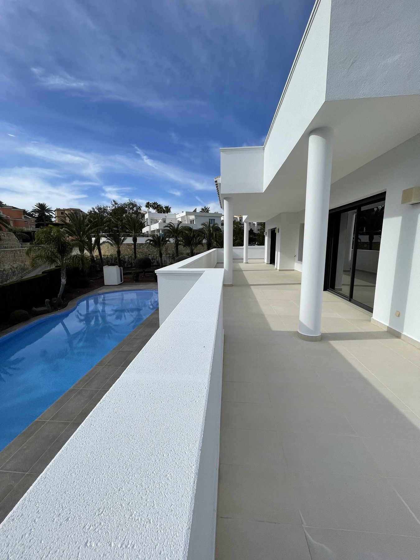 Terraza y peto de piscina recién pintados de blanco con vistas al jardín en villa de Moraira